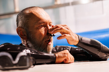 Portrait of senior free diver using nose clip near goggles on poolside 