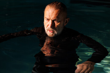 Senior diver in wetsuit standing in swimming pool with light
