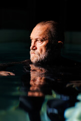 Portrait of grey haired diver swimming in pool with lighting 