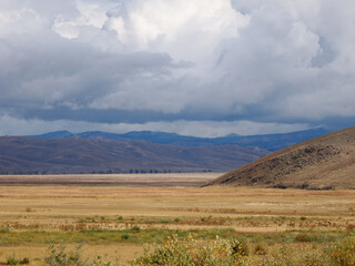 Expansive, arid valley and hills landscape under heavy, dramatic storm clouds