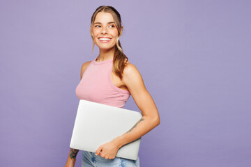 Side view young happy smart IT woman wear pink tank top casual clothes hold closed laptop pc...