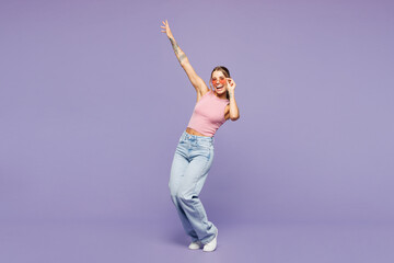 Full body young happy cheerful fun cool woman she wear pink tank top casual clothes sunglasses dance raise up hands isolated on plain pastel light purple background studio portrait. Lifestyle concept.