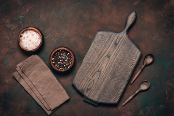 Culinary background with empty wooden board, wooden spoons, spices and linen napkin, dark grunge background, top view, flat lay, copy space