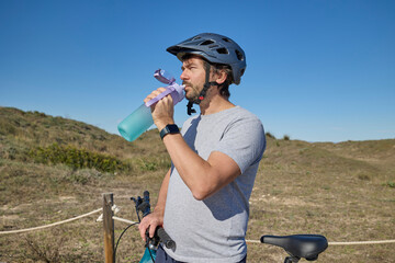 Man wearing a helmet drinking water from a bottle during a cycling break in nature.