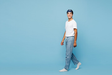 Full body side profile view calm young man he wear pyjamas jam sleep eye mask rest relax at home walk go look camera isolated on plain pastel light blue cyan background. Good mood night nap concept.