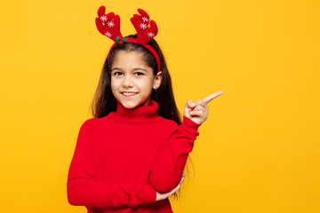Merry little girl wear red clothes fun decorative deer horns on head posing point index finger...