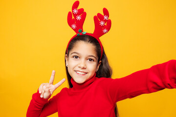 Merry little girl wear red clothes fun decorative deer horns on head posing do selfie pov on mobile...