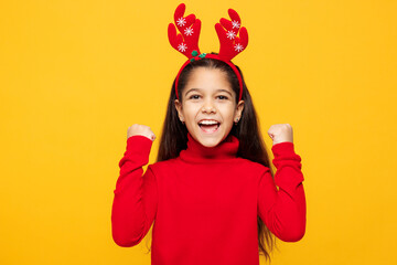 Merry little girl wear red clothes decorative deer horns on head posing do winner gesture celebrate...