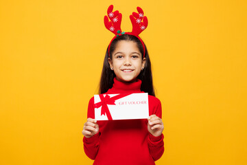 Merry little girl wear red clothes decorative deer horns on head posing hold store gift coupon...