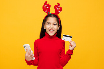 Merry little girl wear red clothes decorative deer horns on head posing using mobile cell phone...