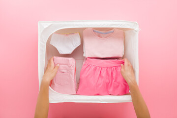 Mother hands folding little child girl clothes. T-shirt, skirt, trousers and panties in white...