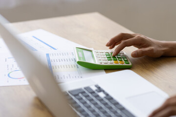 Close-up of Hand Using Calculator with Business Report and Laptop