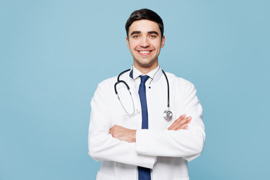 Young male doctor man wears white medical gown suit work in hospital clinic office hold hands crossed folded look camera isolated on plain blue background studio portrait. Healthcare medicine concept.