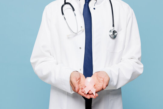 Cropped young male doctor man wear white medical gown suit work in hospital clinic office hold pink ribbon isolated on plain blue background studio Healthcare medicine breast Cancer Awareness concept