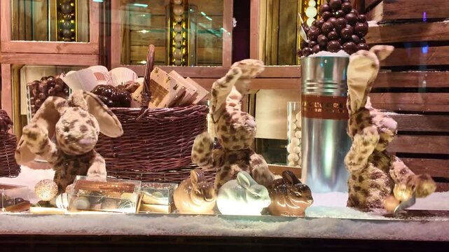 Cute animatronic rabbits moving in a festive Christmas window display. Decorated with chocolates, baskets, and fake snow, this holiday scene attracts shoppers and children