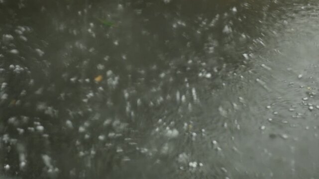 hail falling heavily on asphalt as seen from a vehicle.