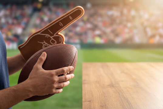 Fan holding football and foam finger at outdoor stadium during game day, cheering support and sports excitement with copy space for promotion or tailgate party concept