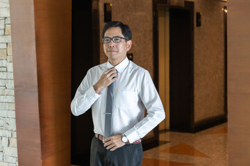 A South East Asian office worker checks his outfit, adjusting his necktie before going to work