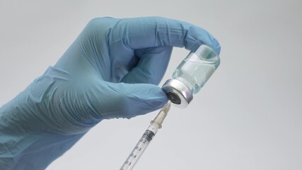 Close-up shot of a healthcare professional in gloves loading a syringe with blue vaccine solution from a vial. Health and medical concepts - Powered by Adobe