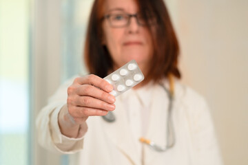 Close-up of a woman doctor holding medication in her outstretched hand. Wearing a stethoscope and...