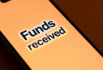 A phone screen displays the phrase "funds received" in bold letters against a warm, bright orange background, highlighting a successful electronic transaction in progress