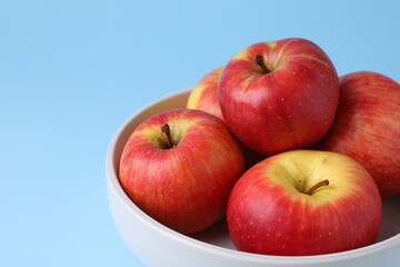 Ripe red apples in bowl on light blue background, closeup. Space for text