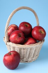 Ripe red apples and wicker basket on light blue background, closeup