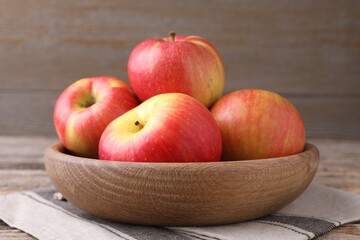 Ripe red apples in bowl on wooden table, closeup