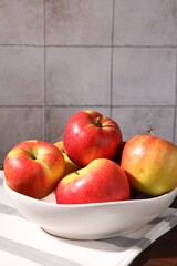 Ripe red apples in bowl on wooden table near grey tiled wall, closeup