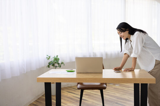 Woman Leaning Over Desk to Look at Laptop Screen