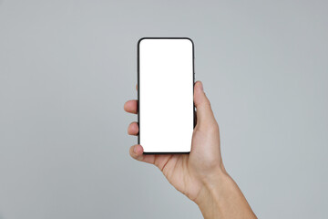 Man holding smartphone with blank screen on grey background, closeup