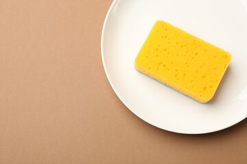 Kitchen sponge and plate on brown background, top view. Space for text