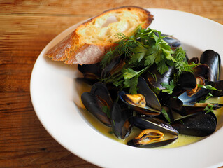 Steamed mussels in white wine sauce with fresh herbs and crusty bread on a rustic wooden table