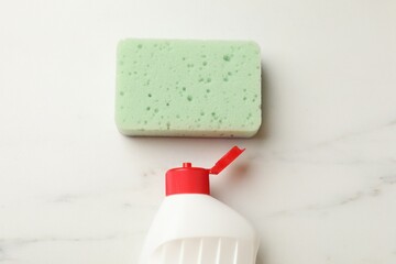 Clean kitchen sponge and dish soap on white marble table, flat lay