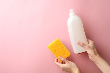 Woman holding sponge and dish soap on pink background, top view. Space for text