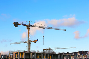 Silhouettes of tower cranes against the blue sky background. House under construction.