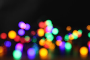 Blurred view of bright Christmas lights on dark background, bokeh effect