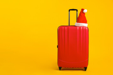 Santa hat on red suitcase against orange background, space for text. Christmas vacation