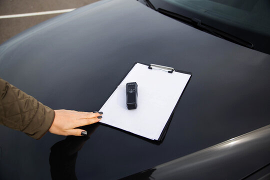 Woman's Hand Points To Breathalyzer On Clipboard. Presenting Sobriety Test Equipment And Documents.