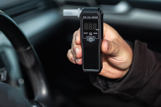 Male Hand Shows Digital Breathalyzer Inside A Car. Driver Holding Sobriety Test Device.