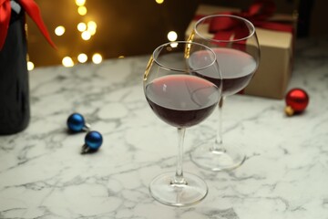 Glasses of red wine and Christmas decor on light marble table, closeup