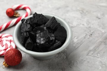Pieces of black coal in bowl, candy cane, lollipop and Christmas baubles on gray textured table, closeup. Space for text