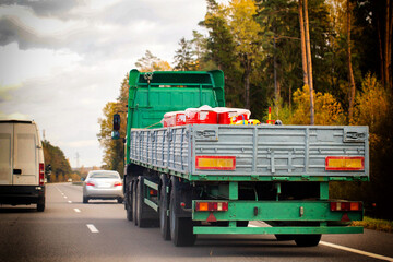 Green semi-truck trailer rear view driving on asphalt highway road through autumn forest landscape under cloudy sky transport cargo vehicle