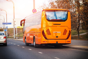 Obraz premium Orange passenger bus parked on side of road during autumn day, rear view of vehicle with bright sunlight