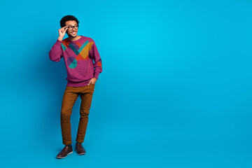 Young fashionable man wearing colorful sweater smiling with hand on glasses against blue background in studio