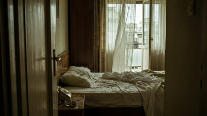 A glimpse through a doorway of a messy, unmade bed in a dark hotel room. A lonely and moody scene of intimacy, departure, or a secret affair.