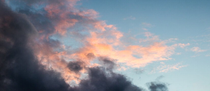 Panoramic view dramatic storm clouds with orange and pink reflections from sunset or sunrise against dark blue sky creating powerful atmospheric background