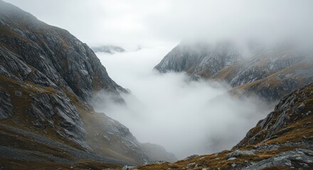 Steep rocky slopes descend into a valley filled with thick white fog under an overcast sky.