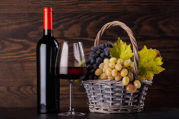 Naklejka premium Red wine bottle with a glass and basket of fresh grapes
