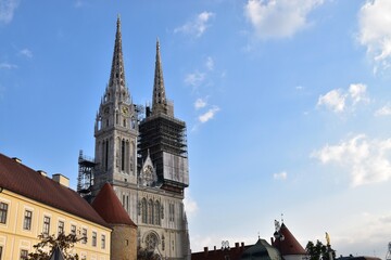 Zagreb Cathedral in Croatia featuring twin neo-Gothic spires with one under renovation scaffolding against a bright blue sky with clouds.